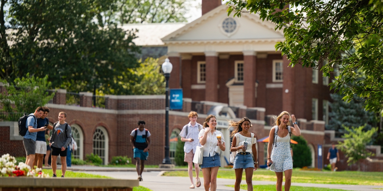 Students walk through Bucknell's campus on a summer day with Coleman Hall behind them.