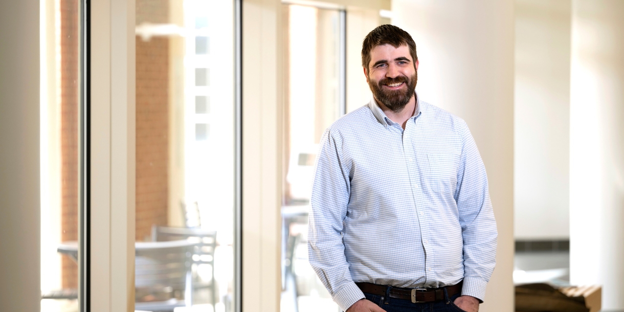 Professor Greg O'Neill wears a button-down shirt and stands and smiles with his hands in his pocket.s