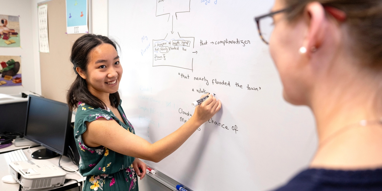 Sanda Tan writes on a whiteboard while Professor Heidi Lorimor stands in the foreground.