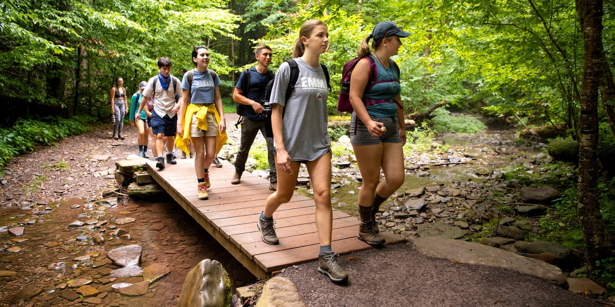Students walking across a small wooden bridge while hiking.