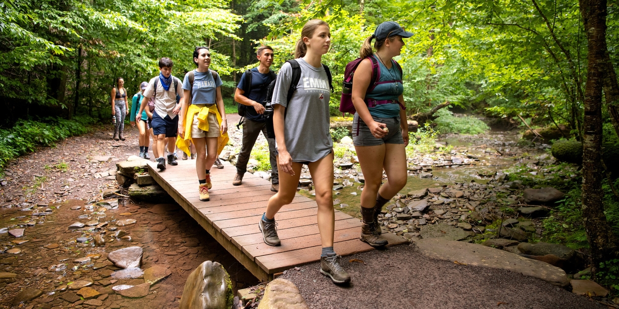 Students walking across a small wooden bridge while hiking. 
