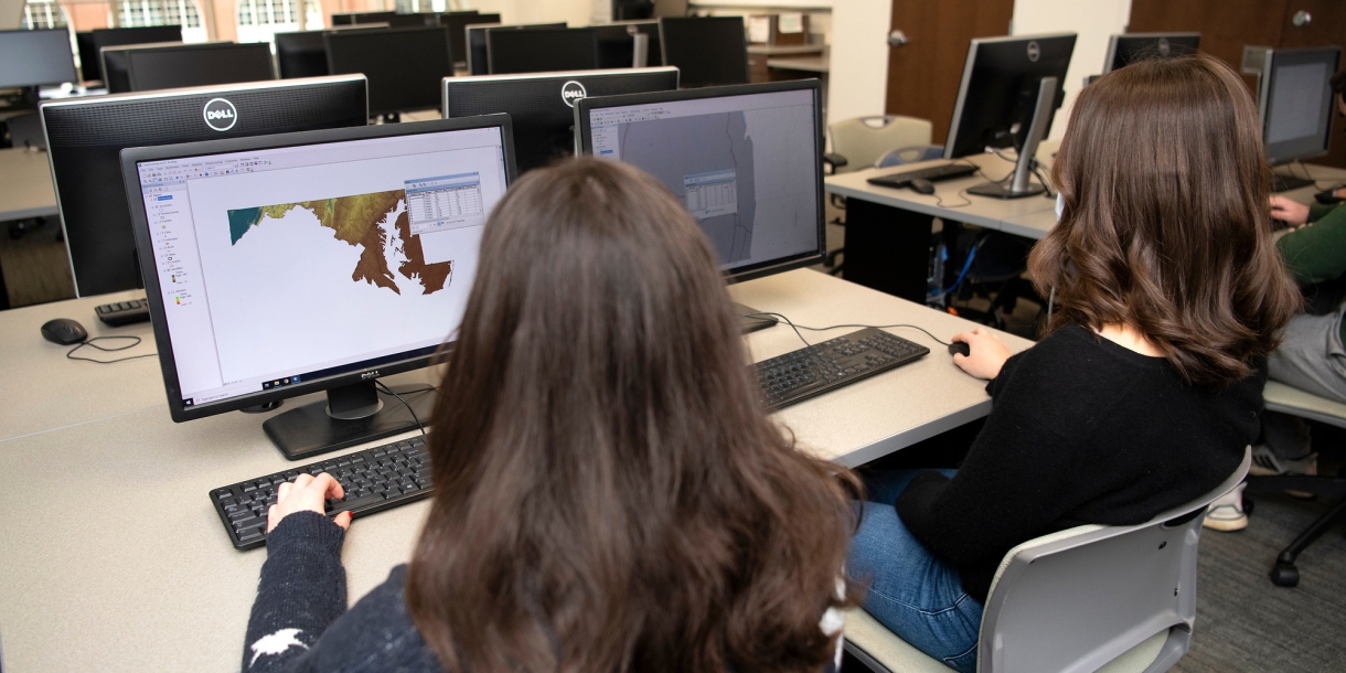 Two students sit and look at maps on their computer