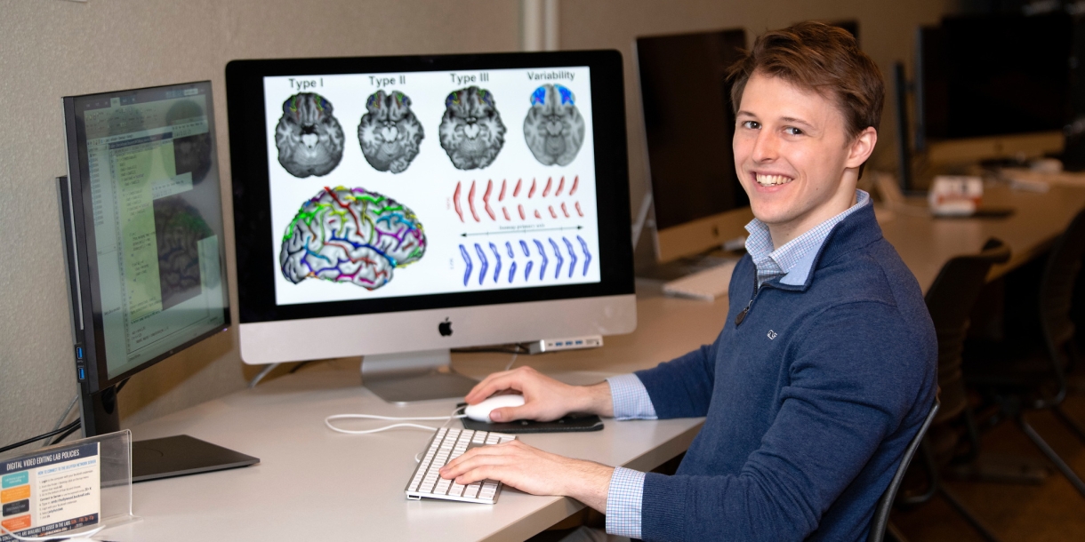 Will Snyder &#039;21 sits at desk with computers displaying brain scans