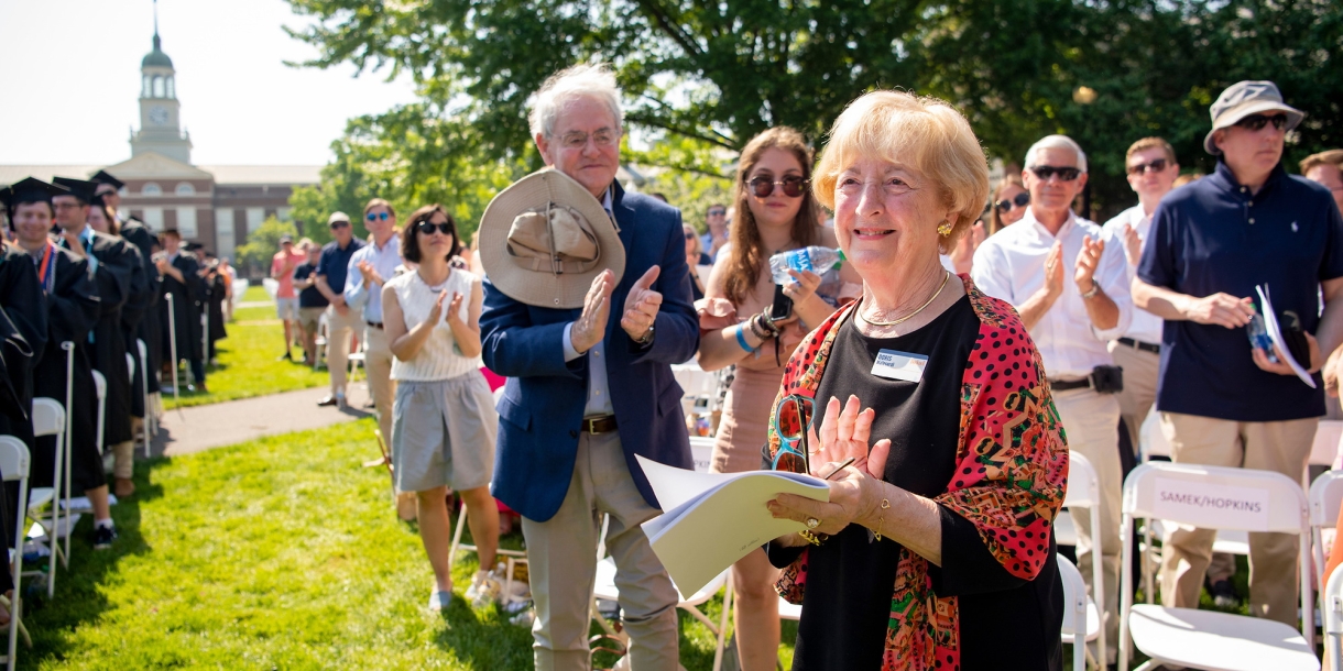 Doris Malesdari S'45 stands and claps and smiles at Commencement, as others in rows behind her also clap and smile.