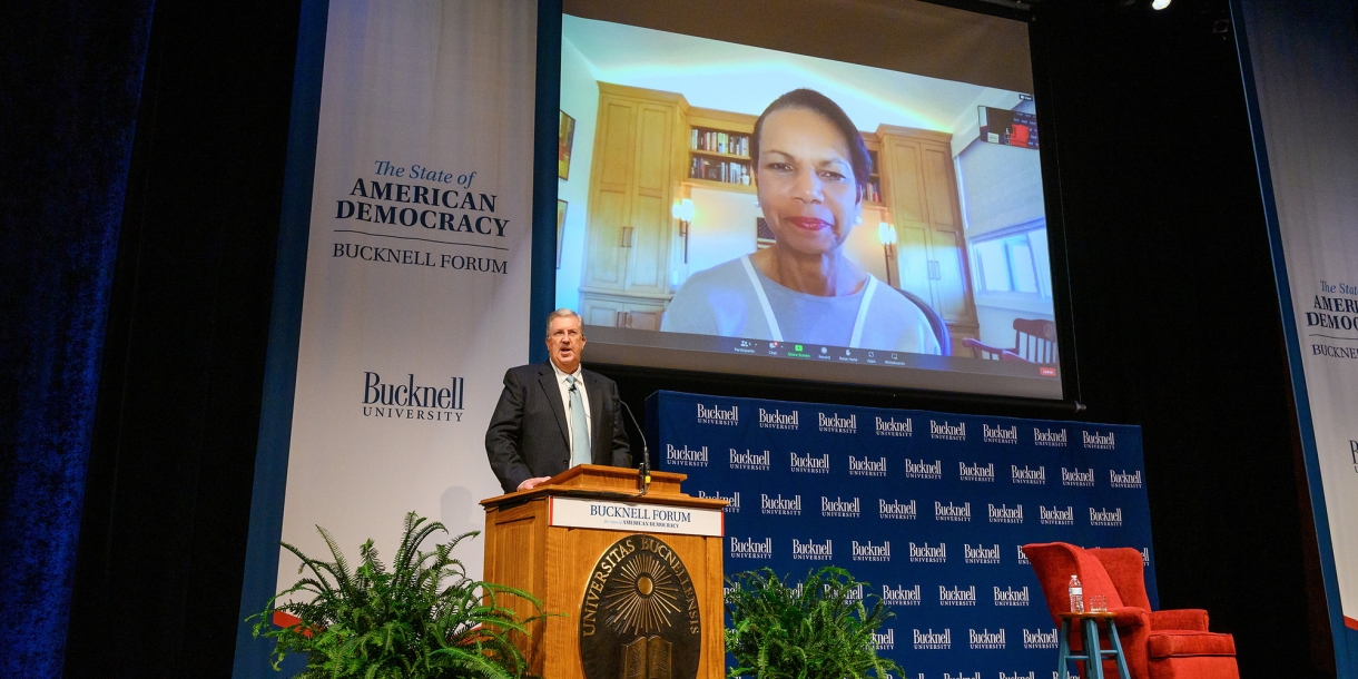 President John Bravman introduces Condoleezza Rice during the Sept. 13 Bucknell Forum event. Bravman stands at a podium with Rice projected on a screen behind him.