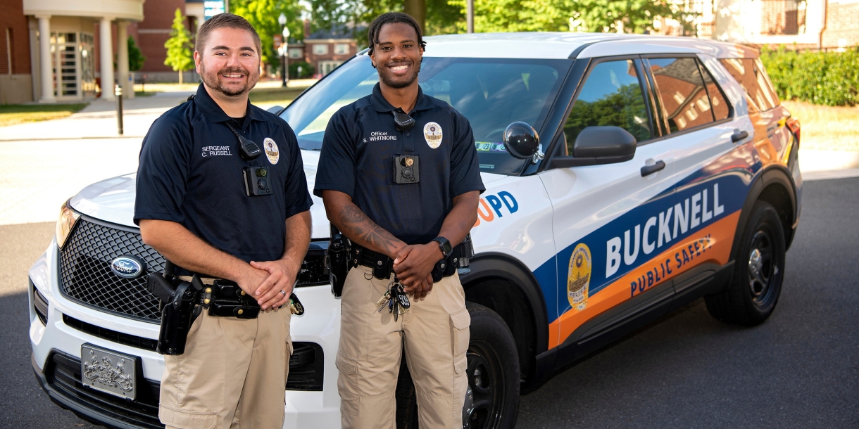 Two Bucknell Public Safety officers pose next to a Public Safety vehicle.