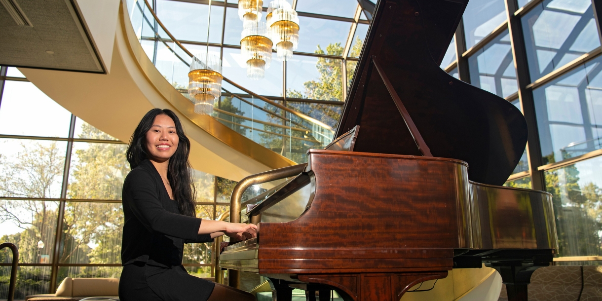 Vivian Kuang sits at a grand piano in a black suit.