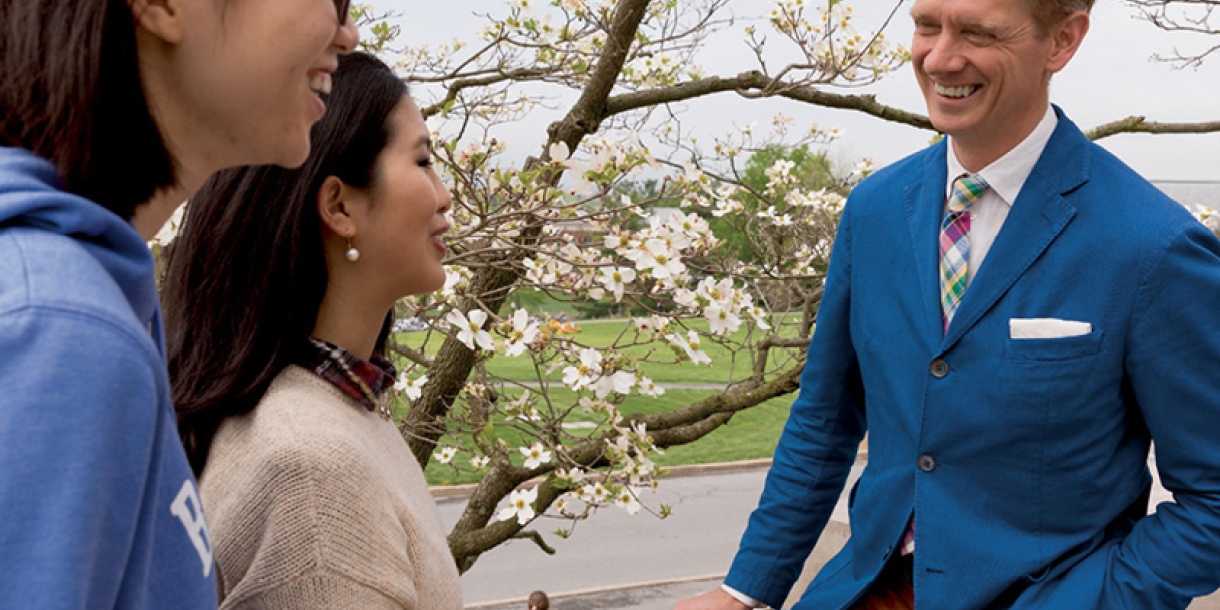 Two students chat with a Communications professor