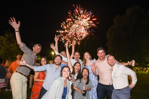 Alumni pose for a photo in front of fireworks