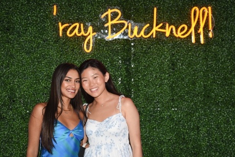 Young alumni pose in front of a "'ray  Bucknell" neon sign.