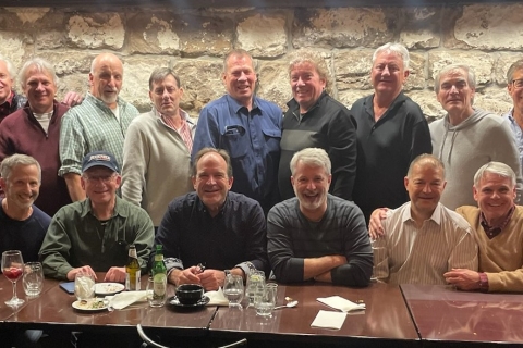 A large group of Bucknellians sit at a table in a long row, while another group of Bucknellians stand behind them.