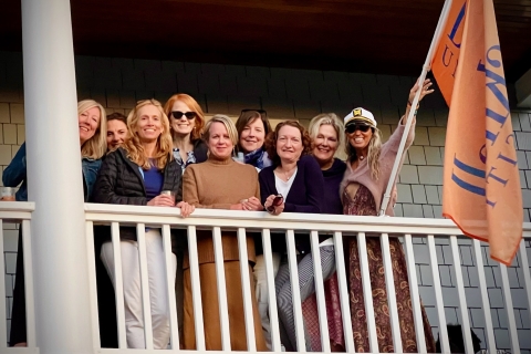 a group of Bucknell alumni stand on a balcony against a railing and smile while holding a Bucknell flag
