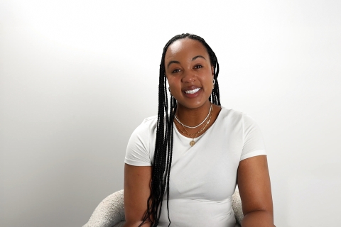 Rebecca Baptiste-Forbes Carter smiles while sitting in a white chair against a white backdrop.