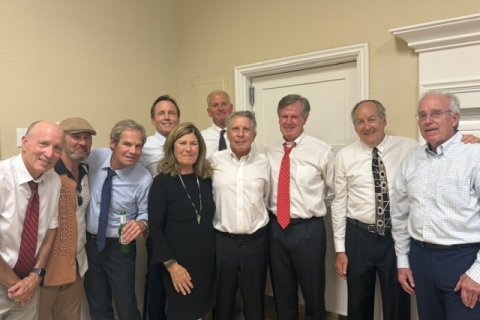 A group of alums, mostly in dress shirts and ties, stand together and smile.