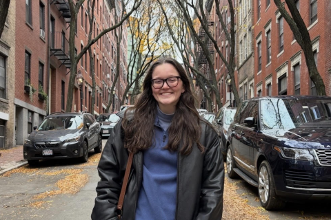 Kona Glenn stands in the middle of a city street with cars parked behind her.