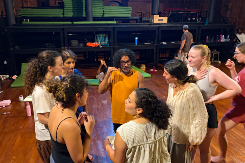 A group of Bucknell theatre students gathers around an instructor during a workshop in a rehearsal space in India.