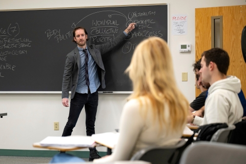 Professor John Penniman, religious studies, points to a blackboard while teaching a class