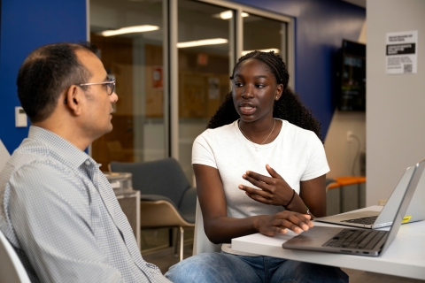 Amanda Agambire &#039;26 sits at a table with her laptop and talks with Professor Rajesh Kumar