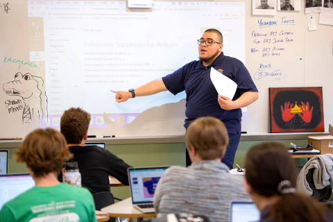 Christian Melgar &#039;23 points to a whiteboard in front of a room of students.