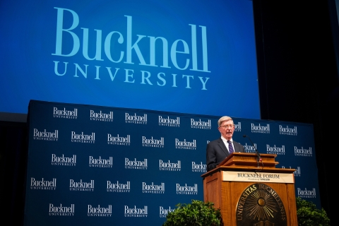 George Will speaks from a podium in front of a &quot;Bucknell University&quot; monogrammed background