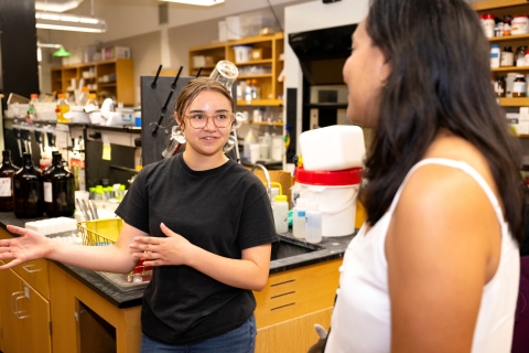 Brianna Bolorin '24 stands in a lab and talks with Jacquelyn Awigena-Cook '05