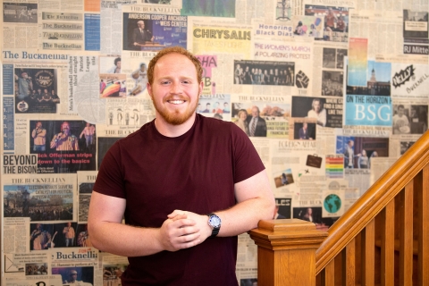 Jaxon White poses in front of a wall of newspaper clippings