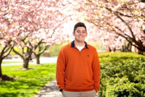 Matthew Vallely &#039;23 poses in front of cherry blossoms.