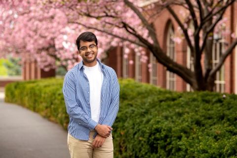Minhaj Bhuiyan stands and smiles in front of a pink cherry blossom tree.