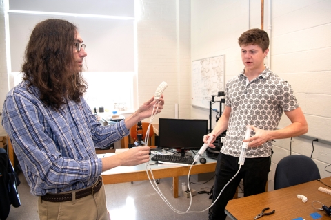 Professor William Scott holds robot spine as Caiden Covell &#039;25 ejects water through it
