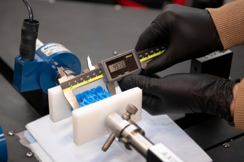 a block of plastic modeled on a sheep's inner horn is inside a piece of testing equipment. Hands measure forces on it using a gauge.