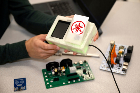 A pair of hands hold the Portal Box, and there are circuit boards on the table.