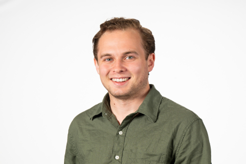 Cole Kratz wears a green button-down shirt and smiles against a white backdrop