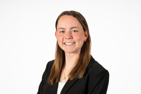 Evvie Hergenhan wears a dark blazer and smiles against a white backdrop.