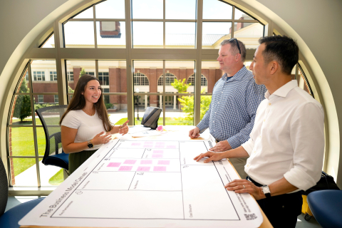 Gianna Sangillo stands at a tall table while speaking to two professors.