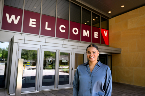 Haden Williams stands outside a building and smiles, "Welcome" is written on the building behind her.
