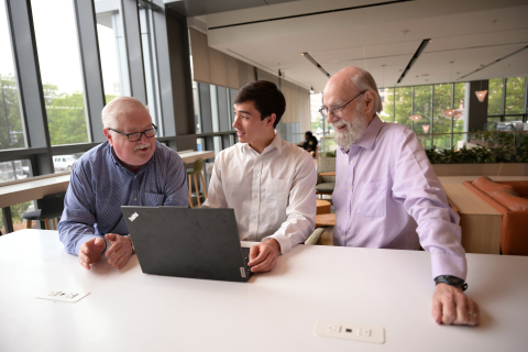 Max Quan is working on a laptop in an office setting with David Hamill to his right and Jack Hoadley to his left.