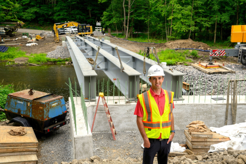 Dominic Viozzi ’27 wears a hard hat and yellow construction safety vest while standing at a bridge construction site.