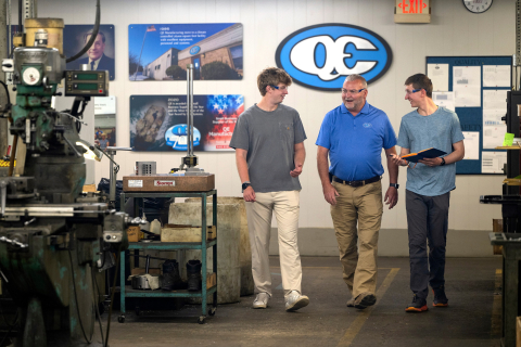 Abbott Spiller and Sam Langlois walk and smile as they talk with a man in a QE facility.