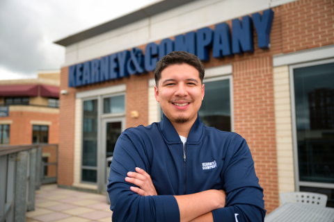 Vincent Torres stands and smiles with arms crossed in front of his body; a Kearney & Company logo is behind him on a brick building.