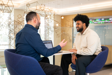 Tony Gomez sits at a table with a laptop and talks with Yosief Tewelde '26 who is smiling.