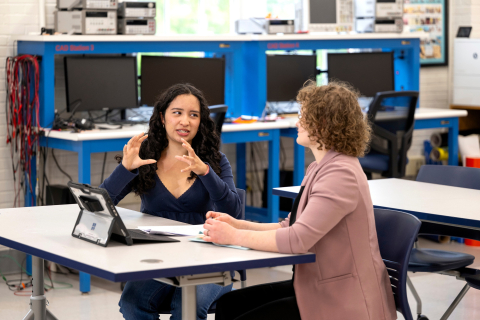 Aura Chuck Hernandez sits at a table conversing with Professor Annie Ross.