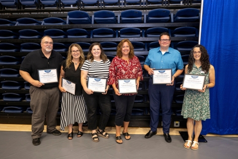 a group of 6 staff members stand together and smile, each is holding a certificate
