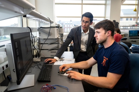 Professor Karlo Malaga interacts with a student sitting and looking at a computer