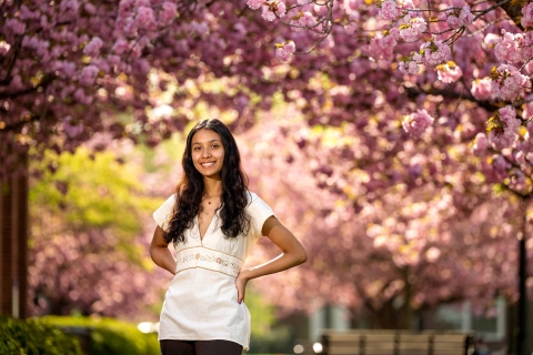 Gabby Diaz '25, in a white dress, poses with her hands on her hips in front of cherry blossom trees.