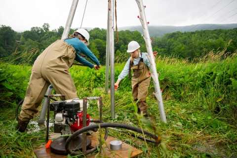 Kira Leclerq and Juliette VanLuven collect a core sample while standing in a field of tall grass