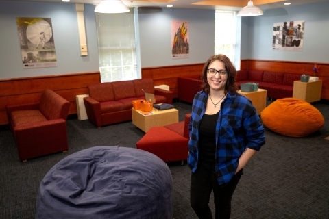 Hannah Kosko stands and smiles in a room that is filled with bright colored chairs.