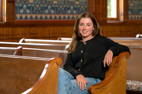 Juliana Capizzi '25, in a black sweater and jeans, sits in a wooden pew in Bucknell Hall.