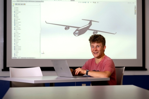 Kade Davidheiser sits in front of a screen that is projecting an image of an airplane on the wall