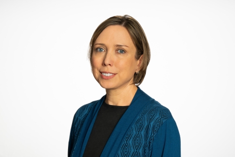 Katie Hays wears a blue jacket over a black shirt and smiles against a white backdrop.