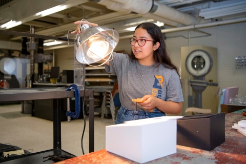 Cindy Cortez points a heat lamp at a model of a building.